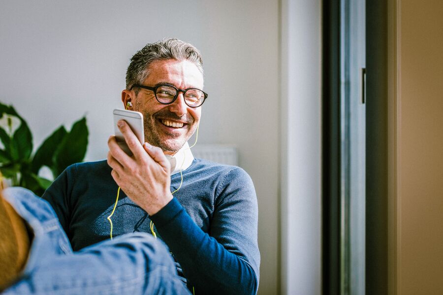 A happy man wearing earphones listens to something from his mobile phone