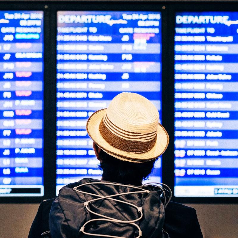 Back view of a man with a hat reading the digital departure flight time boards at the airport