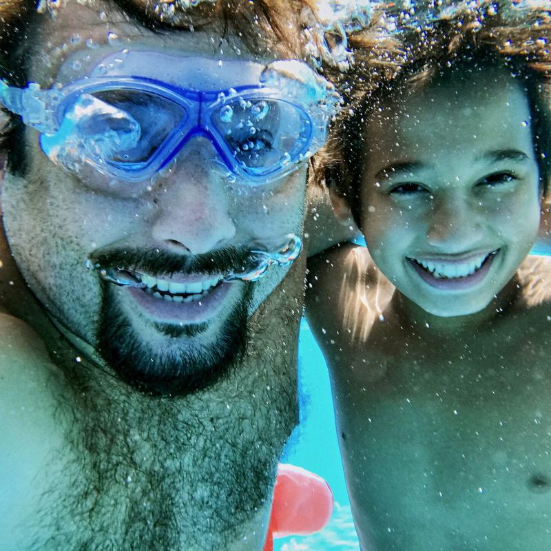 Father and son diving in water and taking selfie