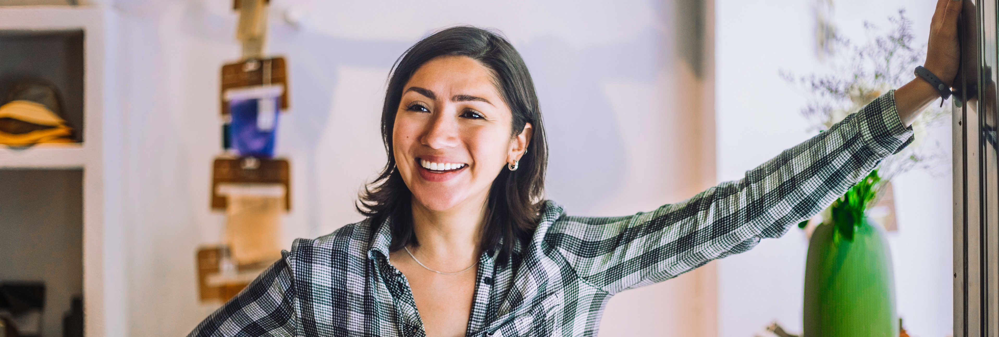 Happy small business owner leaning against a wall in her shop big