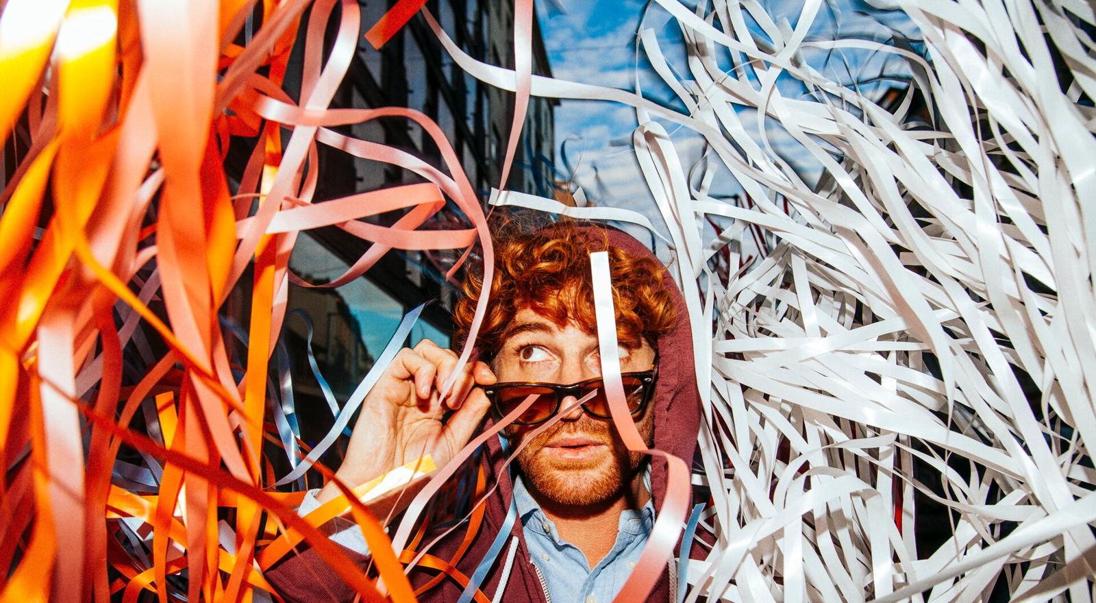 Large Web and Screen A young man removes his sunglasses and looks up while colorful paper streamers fall all around him