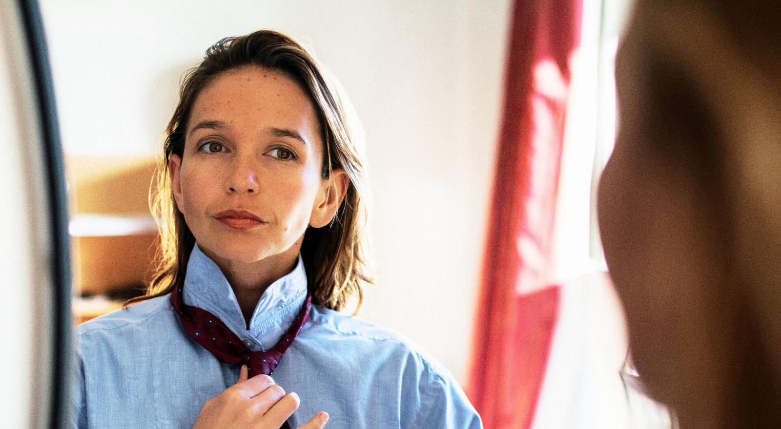Large Web and Screen Portrait of young woman standing before mirror adjusting necktie