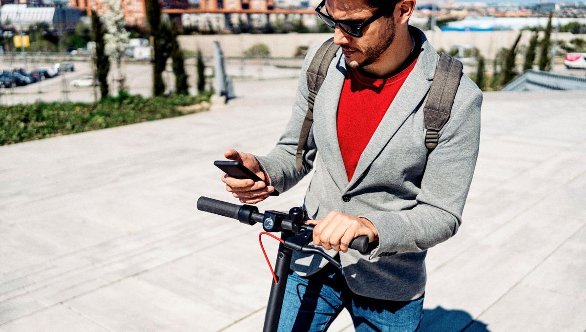 Man riding an e step looks at mobile phone