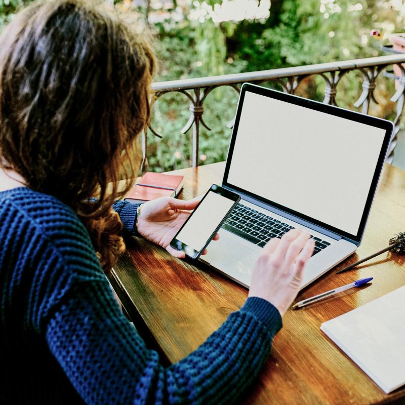 Rear view of a woman using a smartphone and laptop