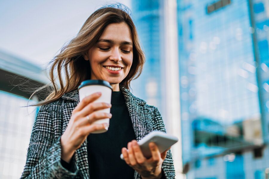 Smiling young woman holding a takeaway coffee looking at her phone 