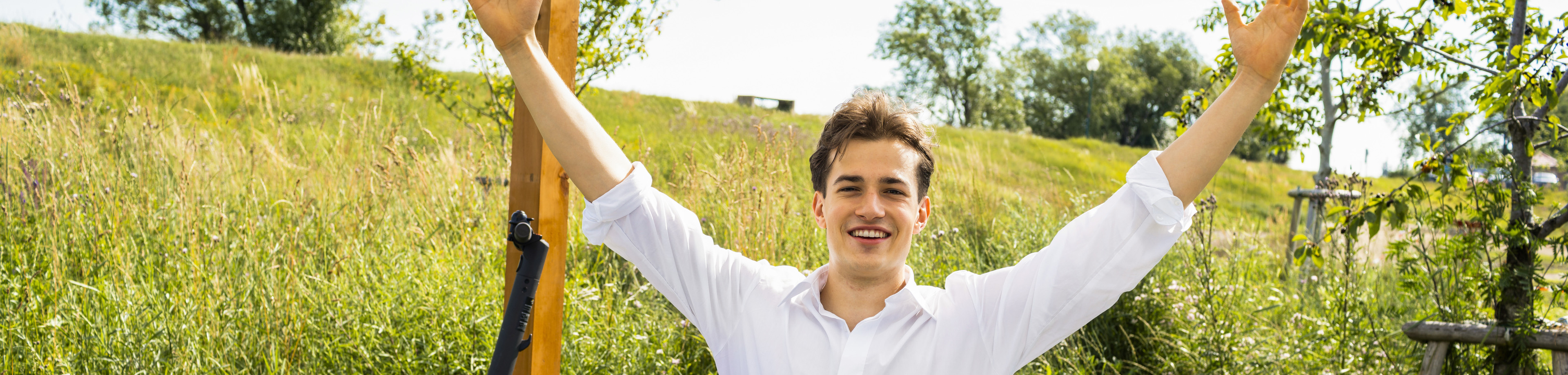 Young man raising his arms outdoors as he works on his laptop at a table